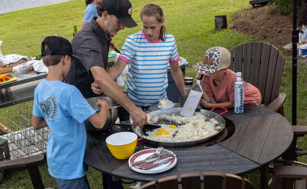 Family cooking rice and eggs together on an outdoor multi-functional grill and griddle.