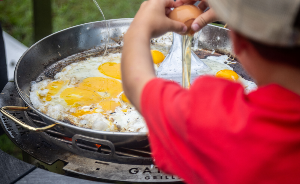 Cracking eggs onto an outdoor griddle, frying breakfast on a stainless steel charcoal grill